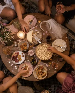 Mesa de centro vista de cima numa despedida de solteira em casa, com petiscos, bolo e a tiara de véu da noiva