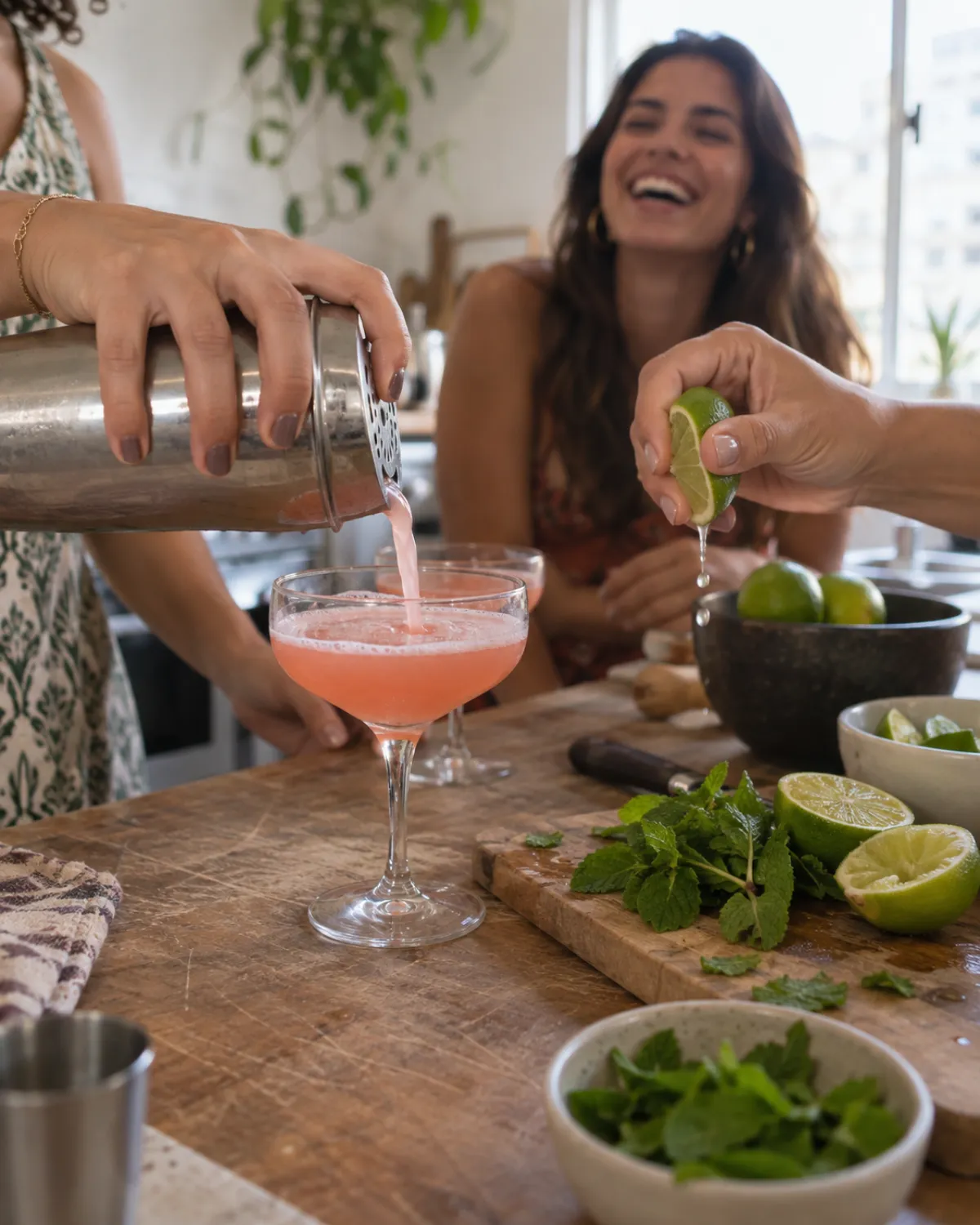 Mãos preparando drink rosa com coqueteleira e limão numa oficina de drinks em casa