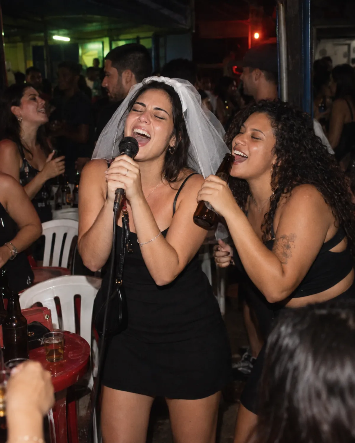 Noiva de véu cantando no karaokê de um bar com uma amiga cantando junto