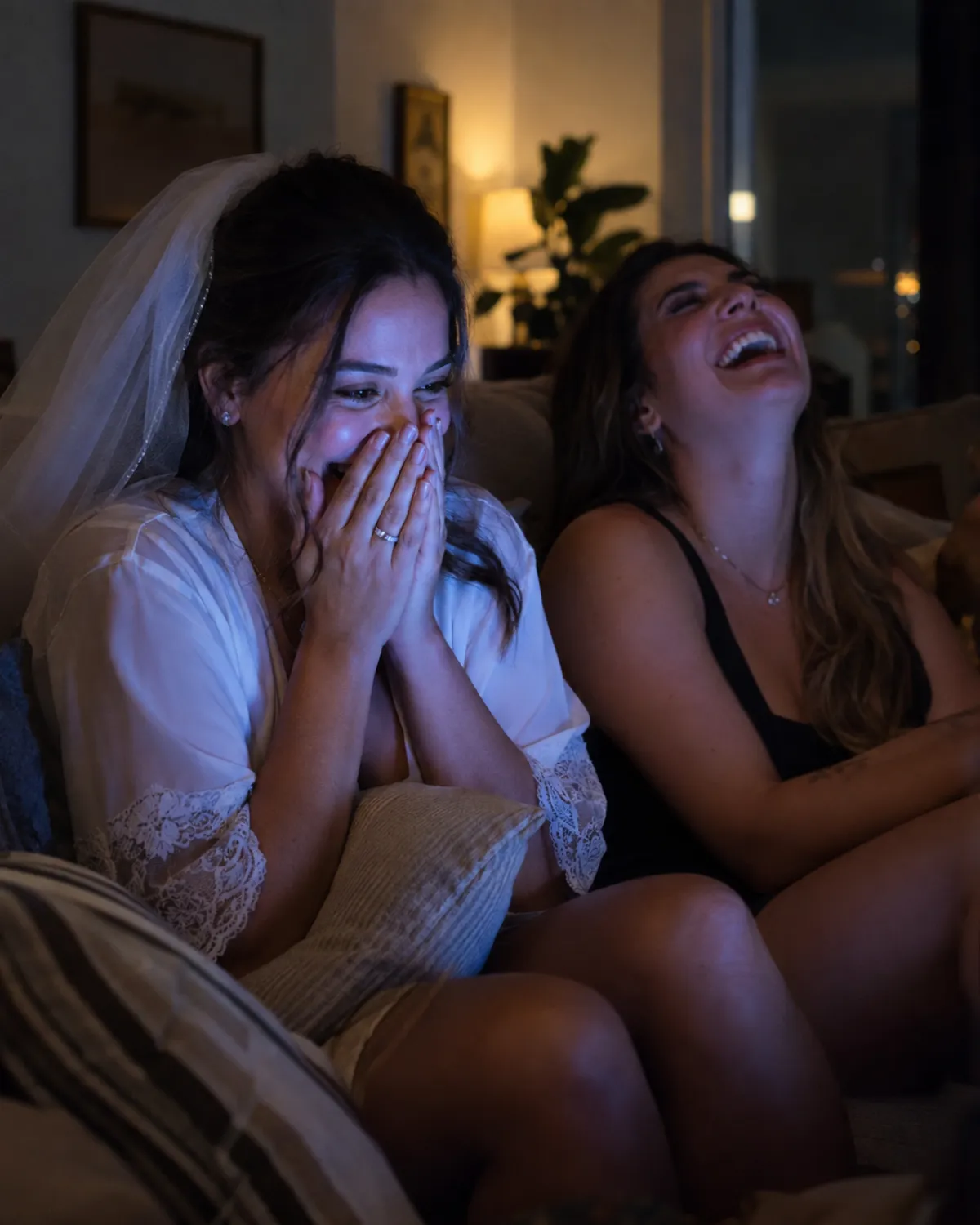 Noiva com as mãos no rosto rindo ao assistir ao vídeo do noivo ao lado de uma amiga