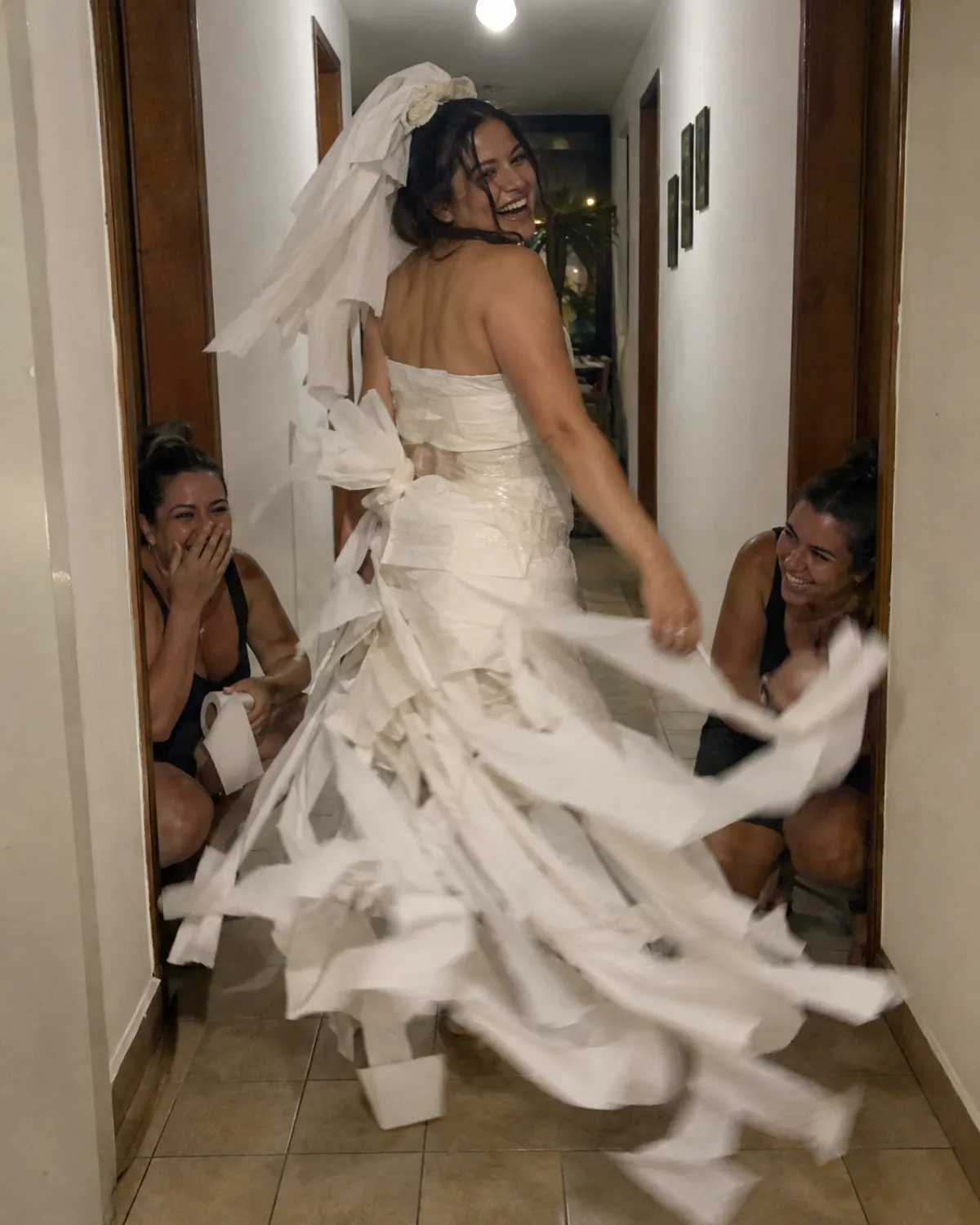Amiga girando com vestido de noiva de papel higiênico no corredor enquanto as outras riem