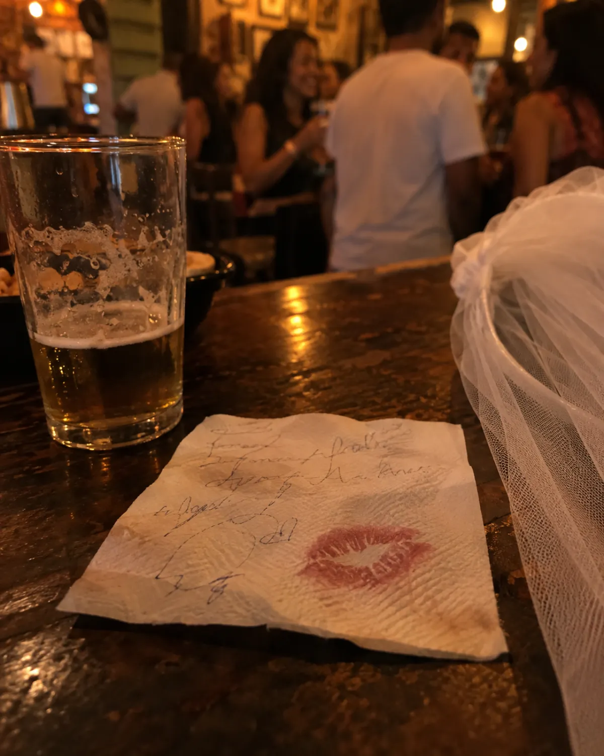 Guardanapo com recado escrito e marca de batom no balcão do bar, ao lado do véu da noiva