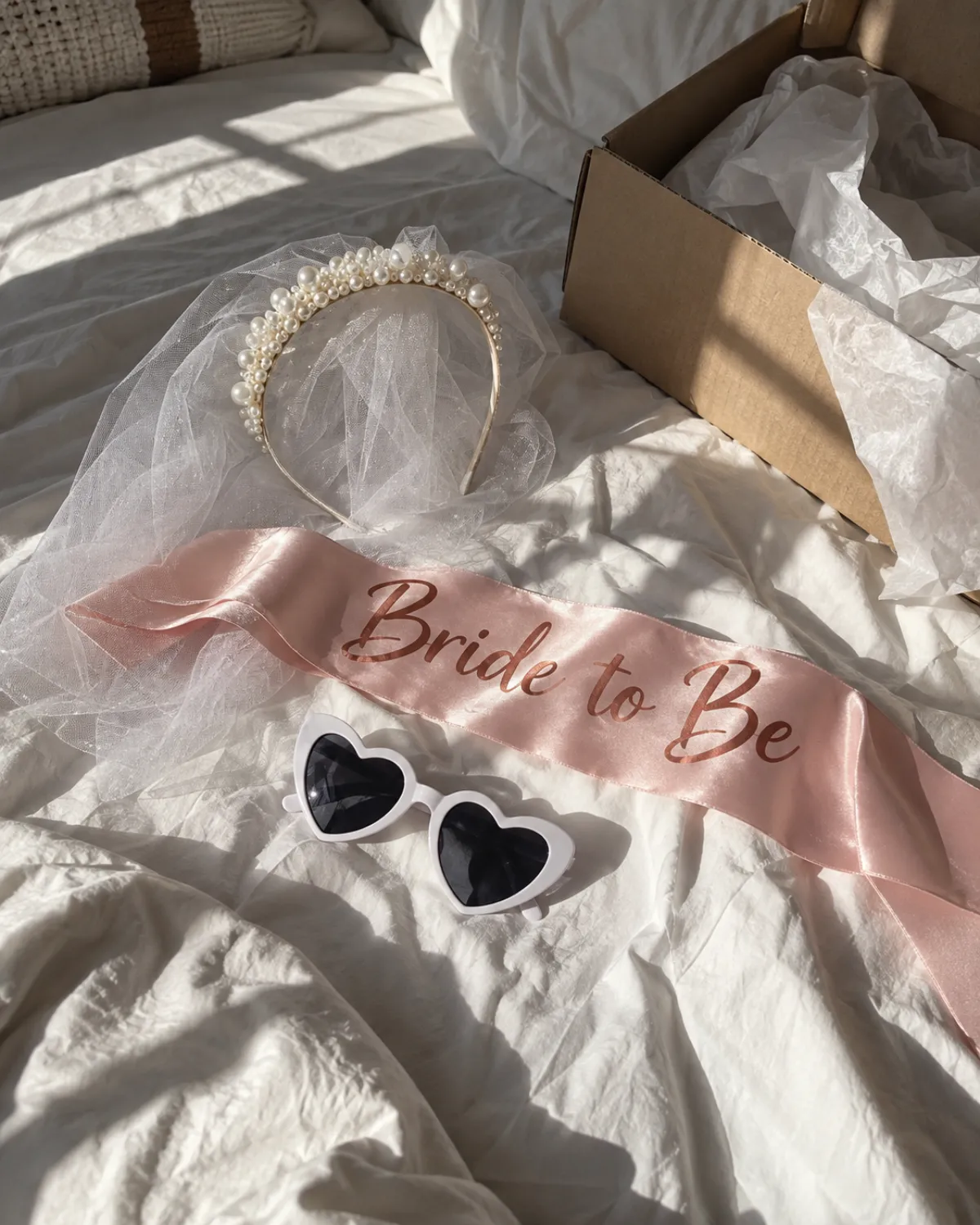 Tiara de pérolas com véu, faixa Bride to Be e óculos de coração sobre a cama